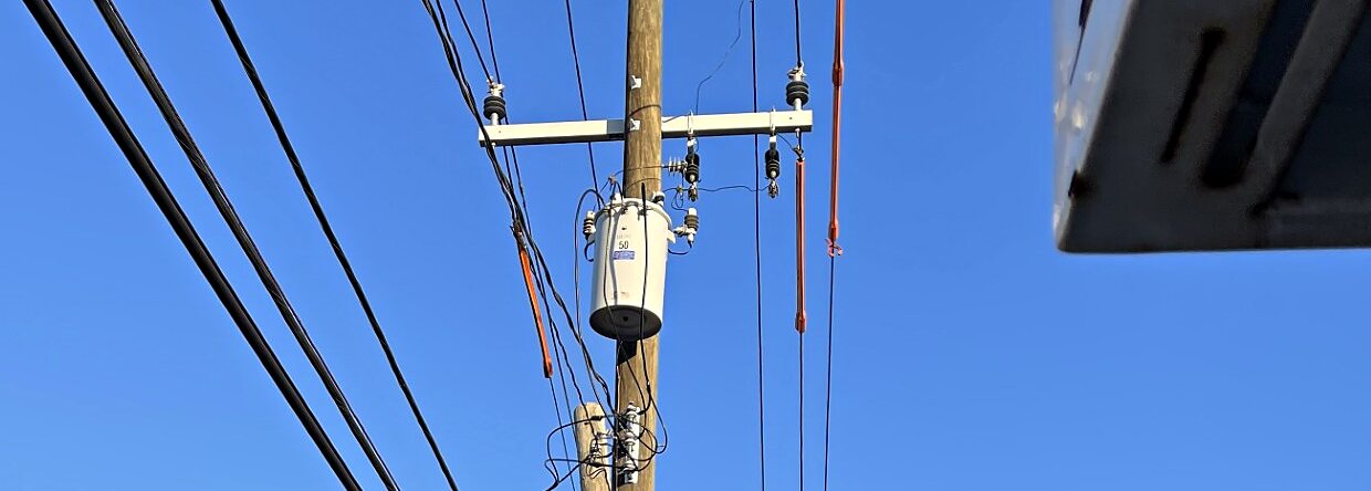 Pole-mounted distribution transformer, crossarm insulators, and a bucket boom alongside on an overhead distribution job