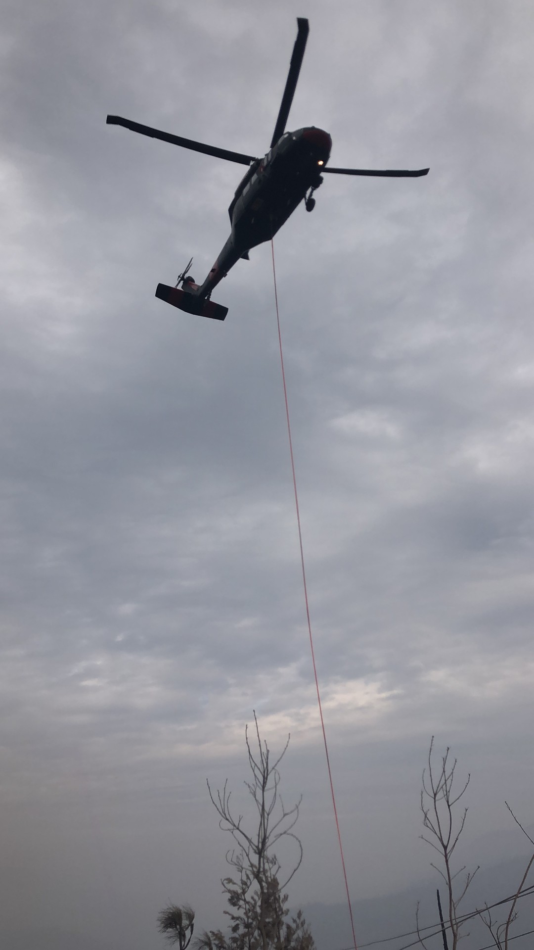 Helicopter flying a long line over a utility right-of-way during aerial line work