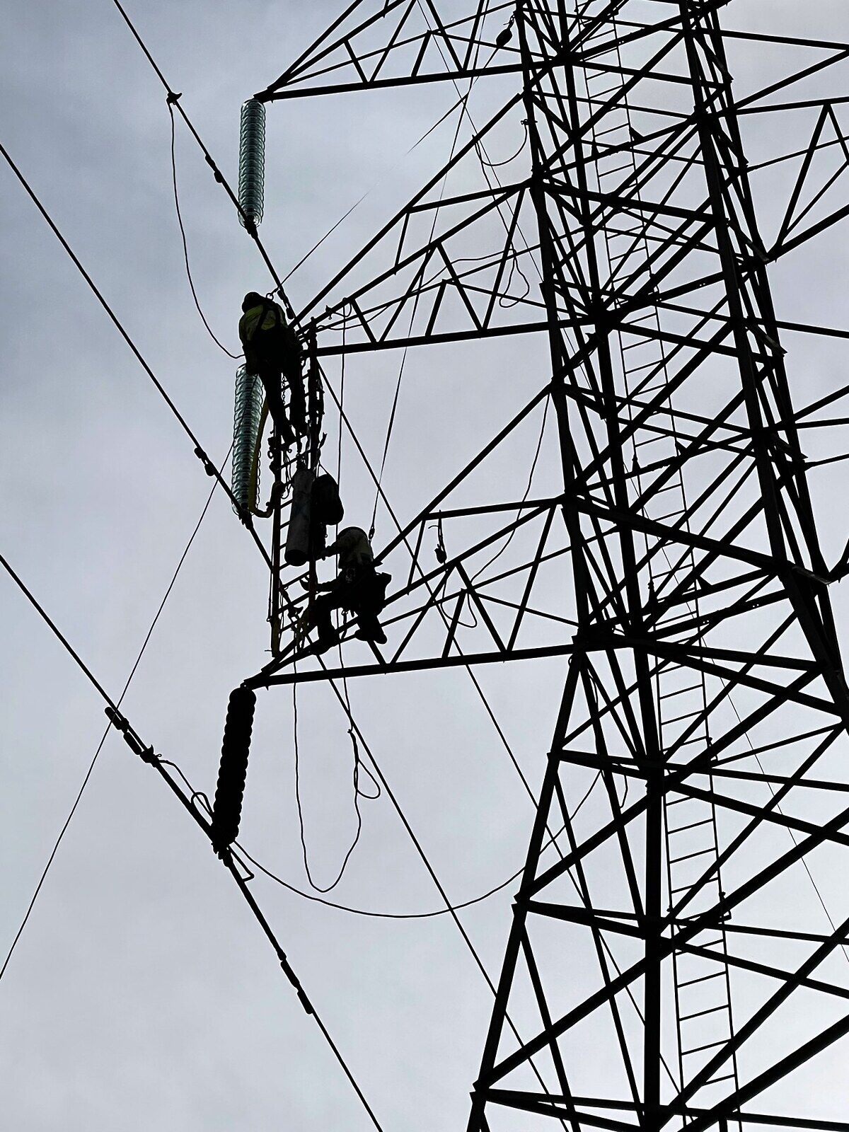 Two linemen working high on a steel transmission tower