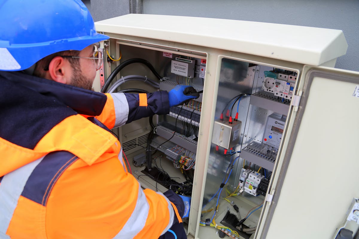 Lineman in hard hat, safety glasses, hi-vis jacket, and insulated gloves performing safe maintenance on an underground padmount transformer cabinet